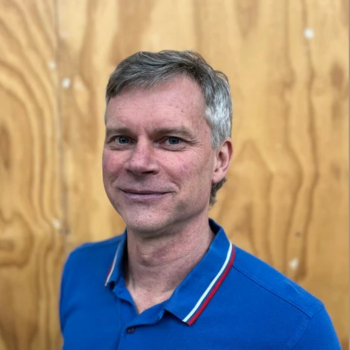 Man in blue polo shirt smiling against wooden wall background
